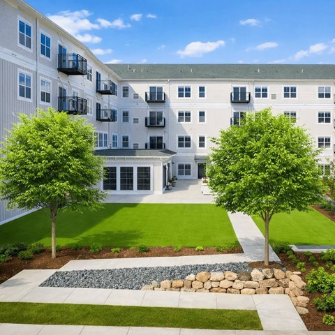 A large white building with balconies and a green lawn in front.