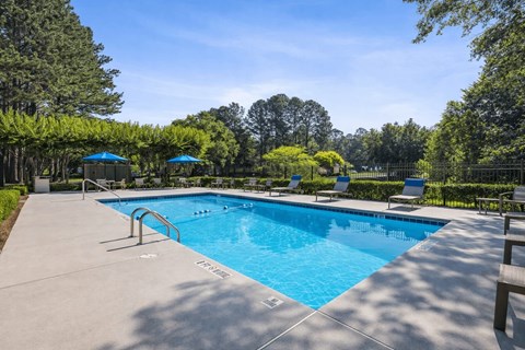 A large outdoor swimming pool surrounded by trees and lounge chairs at Emerald Pointe, Riverdale, Georgia