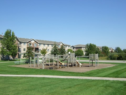 A playground with swings and slides in front of apartment buildings.