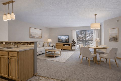 A well-lit, modern kitchen and living room with wooden furniture and a large window.