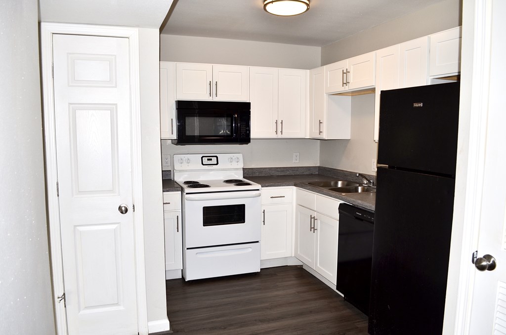 A black refrigerator is in a kitchen with white cabinets at The Wilshire Apartment, Lake Charles, 70607