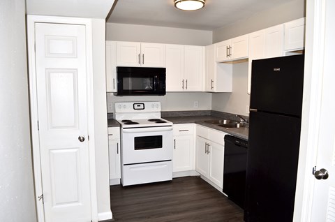 A black refrigerator is in a kitchen with white cabinets.