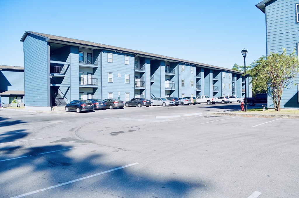 A parking lot in front of a blue building with cars parked. A parking lot in front of a blue building with cars parked at The Wilshire Apartment, Lake Charles, LA, 70607