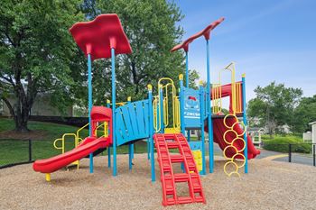 A playground with a blue and yellow slide, red and yellow climbing frame, and a red and blue climbing tower.