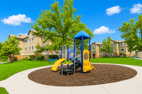 A playground with a blue and yellow slide in the middle of a circular play area at Slate Canyon Apartments, Utah, 84606