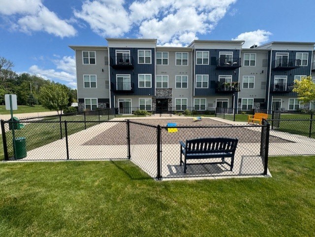 a bench in a fenced in park in front of an apartment building