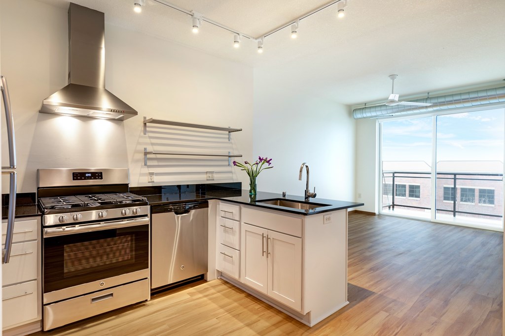 A modern kitchen with a stainless steel range hood and black countertops.