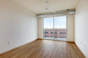 A room with wooden floors and a sliding glass door leading to a balcony.