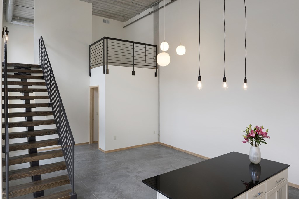 A room with a staircase, a table with a vase of flowers, and hanging lights.