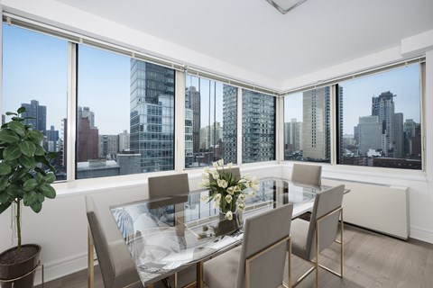 A dining room with a glass table and chairs with a view of the city.