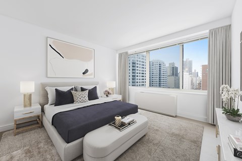 A bedroom with a large bed and a city view through the window.