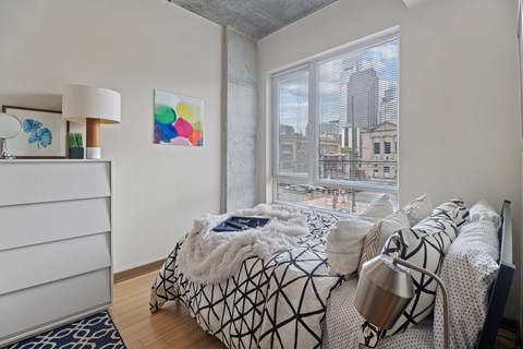A bedroom with a large bed and a city view through the window.