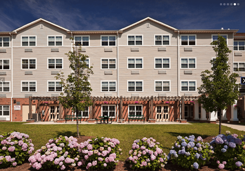 A large apartment building with a flower bed in front.
