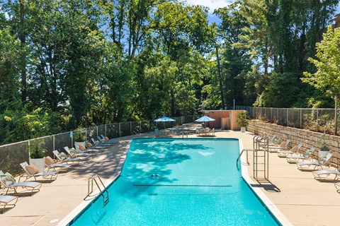 A large swimming pool surrounded by trees and chairs.