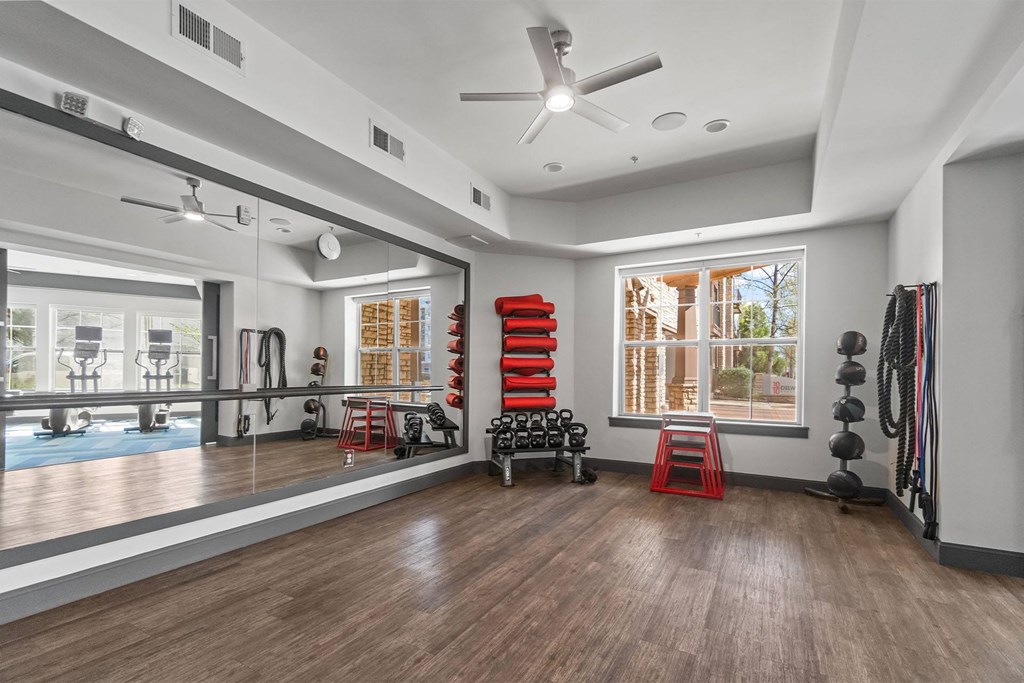 A spacious room with a ceiling fan, exercise equipment, and a view of the outdoors through large windows. at 1010 Dilworth Apartments, Charlotte, NC, 28204