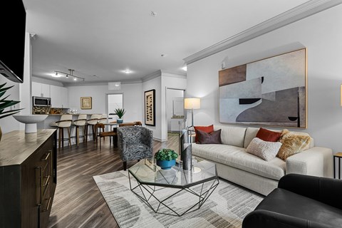 A modern living room with a white sofa, a glass coffee table, and a large abstract painting on the wall.