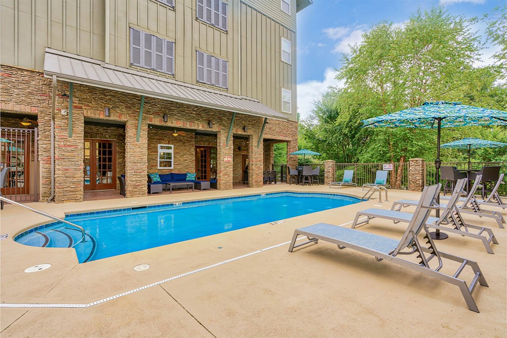 A pool with sun loungers and umbrellas in front of a building at The Lofts at Reynolds Village Apartments, Asheville 92627