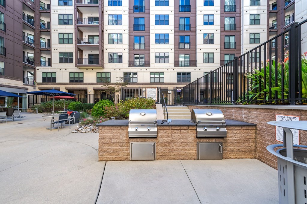 A patio with barbecue grills and a building in the background at The Edison Lofts Apartments, Raleigh, 27601