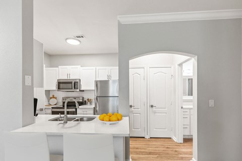 A kitchen with white cabinets and a white island with a bowl of lemons on it.
