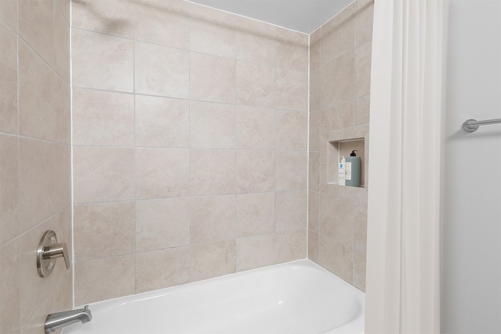 a bathroom with beige tiles and a white bathtub at Padonia Village Apartments, Timonium MD
