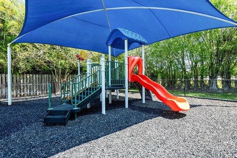 A playground with a blue umbrella and a red slide at Waterview at Coconut Creek, Coconut Creek, FL
