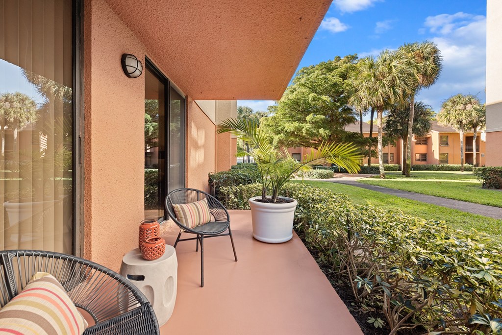 a balcony with two chairs and a table and a yard with palm trees