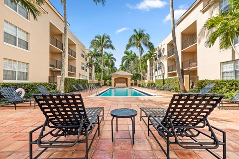 a pool area with chairs and a table in front of an apartment building