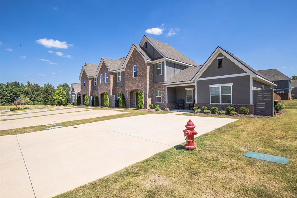 A red fire hydrant sits on a green patch of grass in front of a grey house.