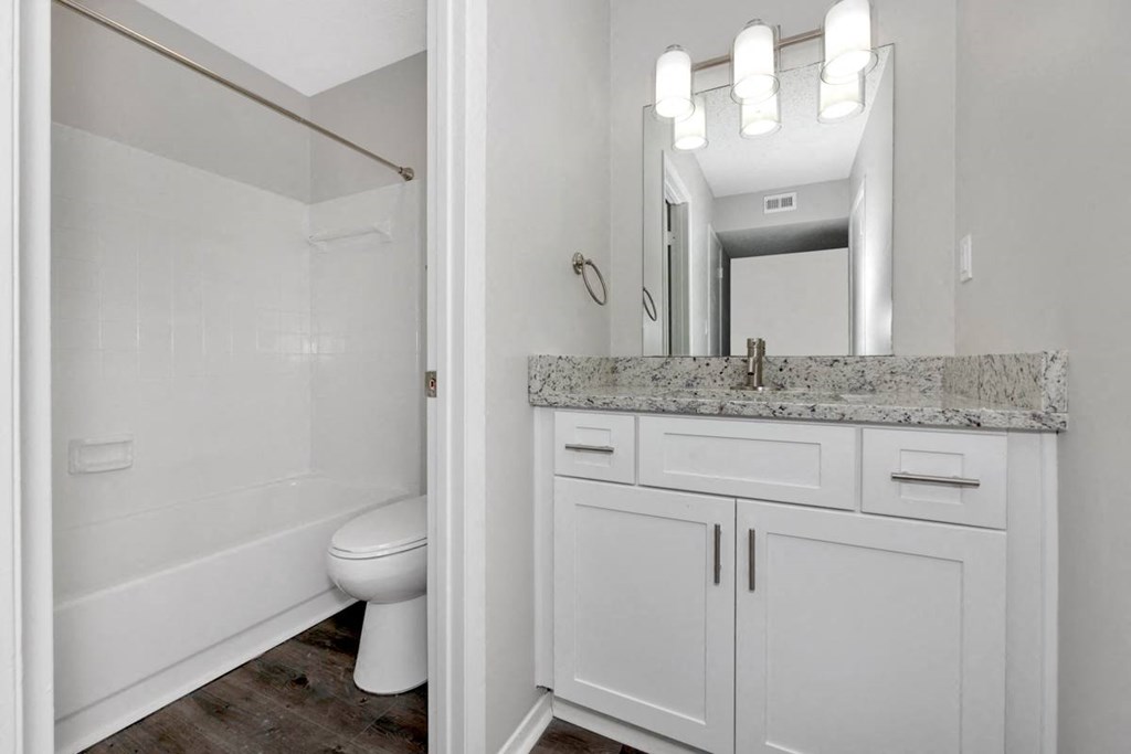 A white bathroom with a marble counter top and a large mirror.