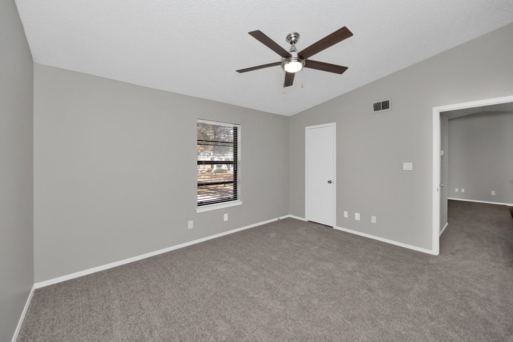 A room with a ceiling fan and a window with a view of a tree.