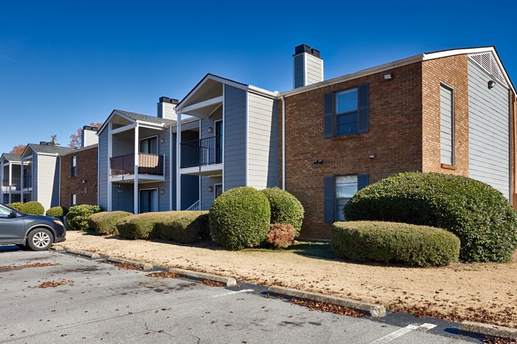 A grey car is parked in front of a building with a blue sky in the background.