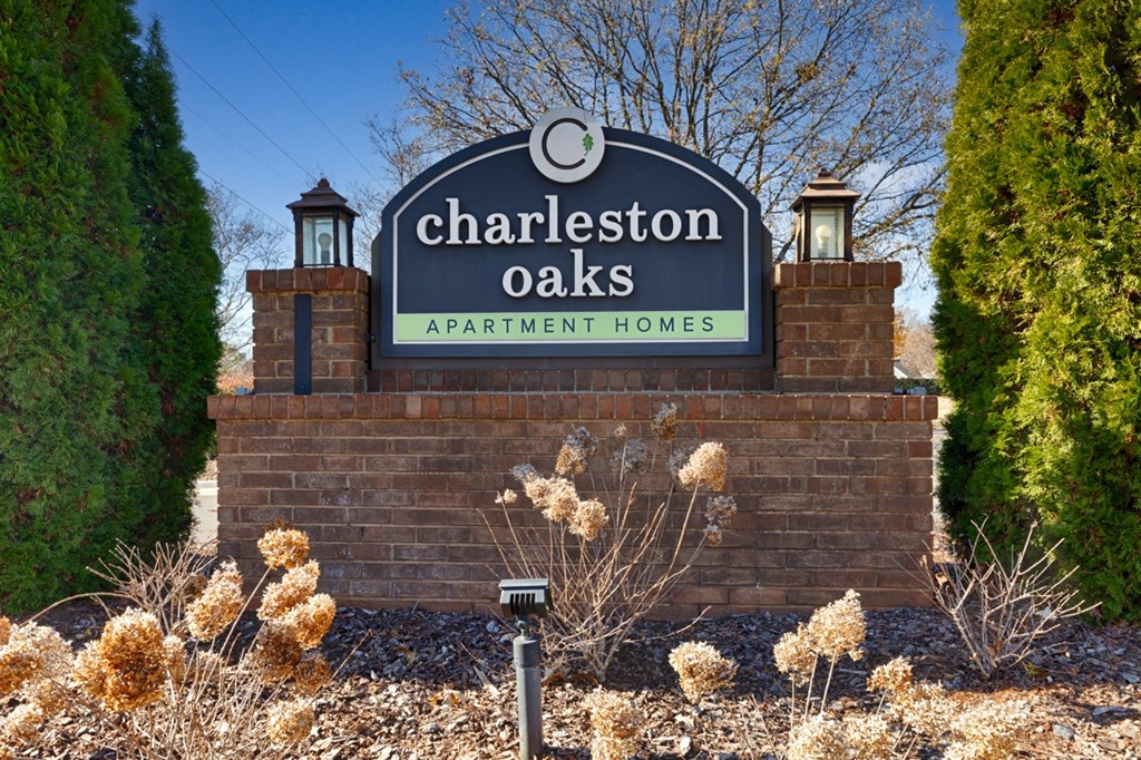 A sign for Charleston Oaks Apartment Homes is displayed in front of a brick wall.