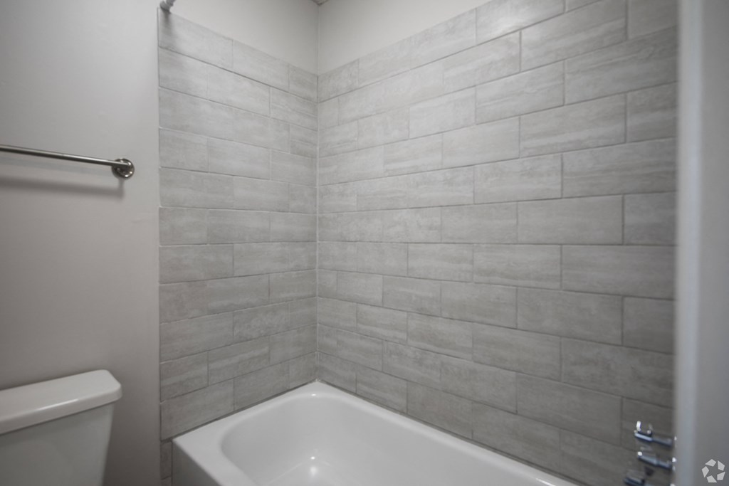 A white bathtub sits in a bathroom with a grey tiled wall.
