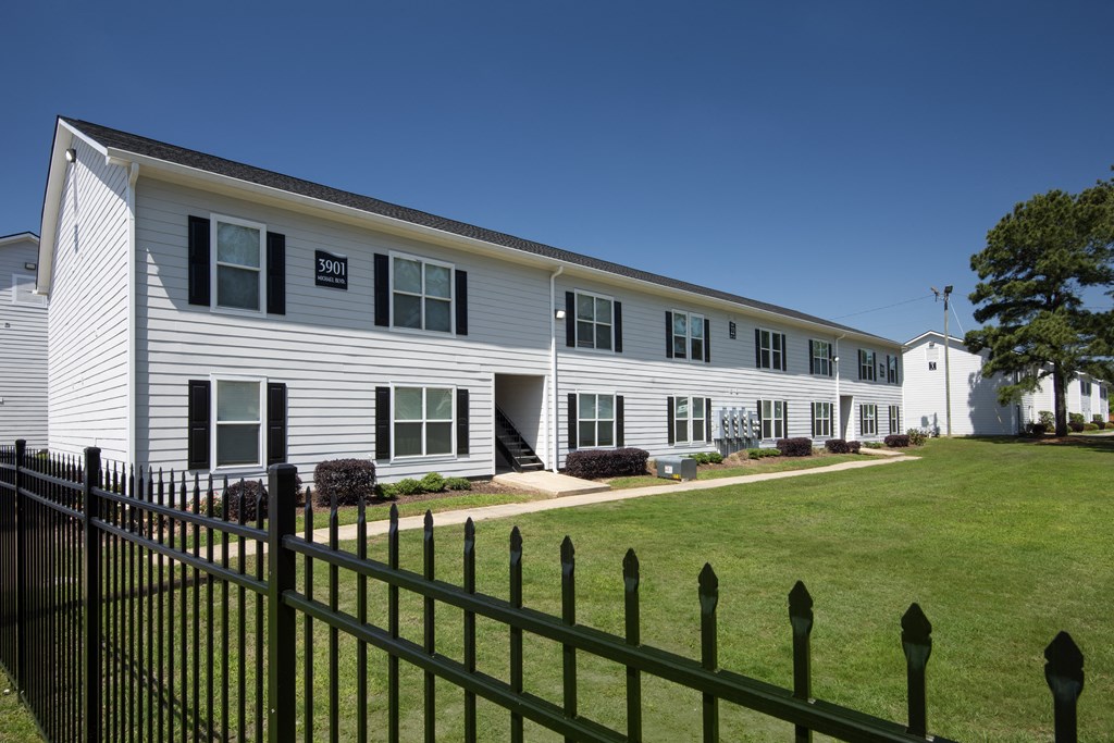 a white house with a green lawn and a black fence