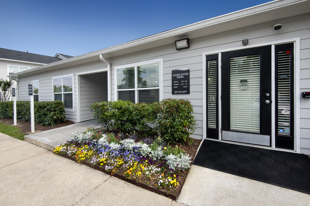 the front of a white house with a garden of flowers