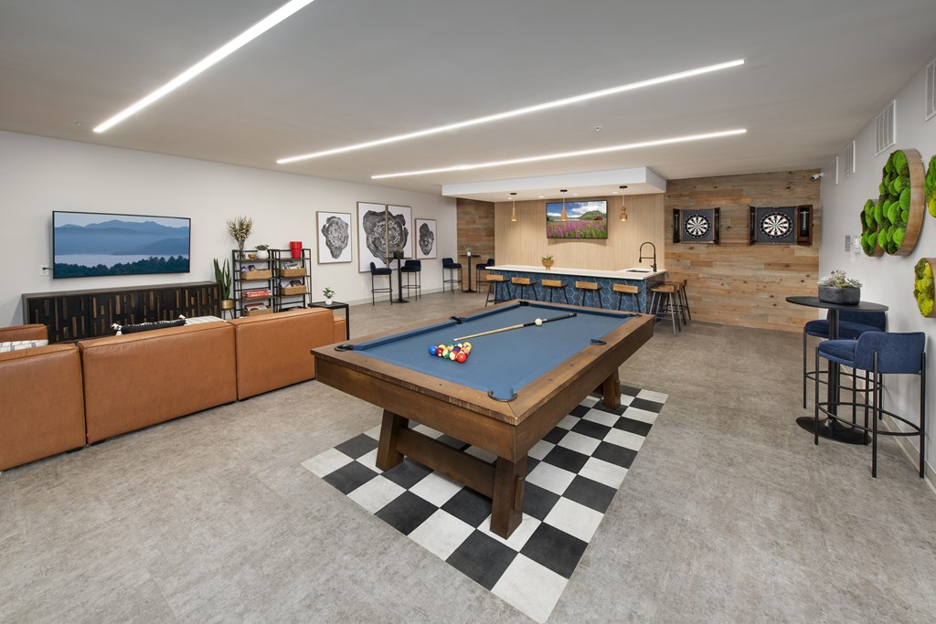 A pool table is in the middle of a room with a bar and a television.