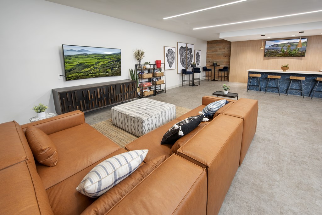 A living room with a brown leather couch and a television on the wall.