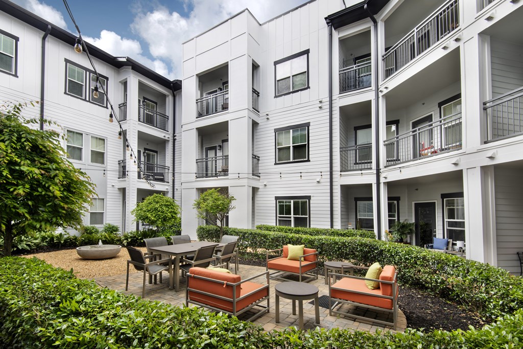 A patio with a table and chairs is surrounded by a well-kept garden in front of a white apartment building.