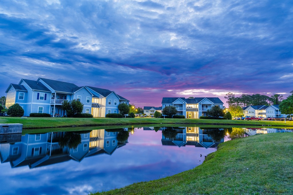 a pond in front of a row of houses at sunset