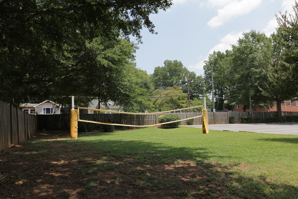 a volleyball net in a grassy area with trees and an apartment building in the background