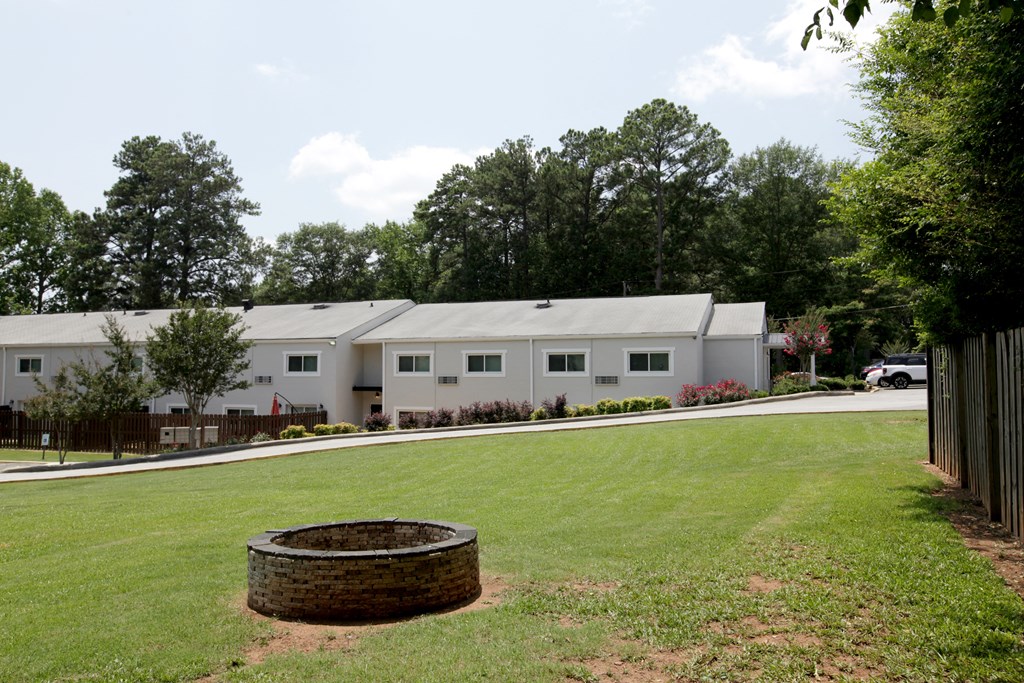 a fire pit sits in the middle of a grassy field in front of a white building