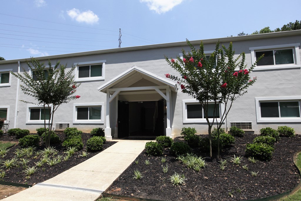 a gray building with a sidewalk and trees in front of it