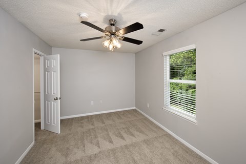 an empty bedroom with a ceiling fan and a window