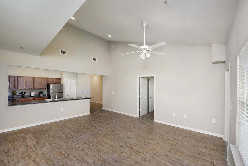an empty living room with a ceiling fan and a kitchen