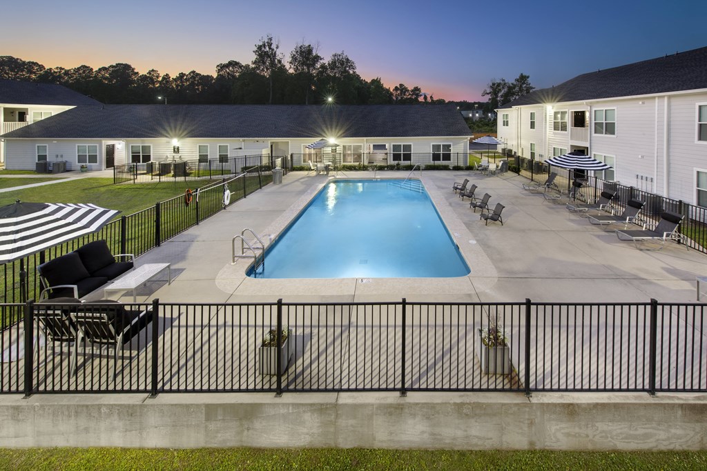 a swimming pool with chairs and tables around it at night