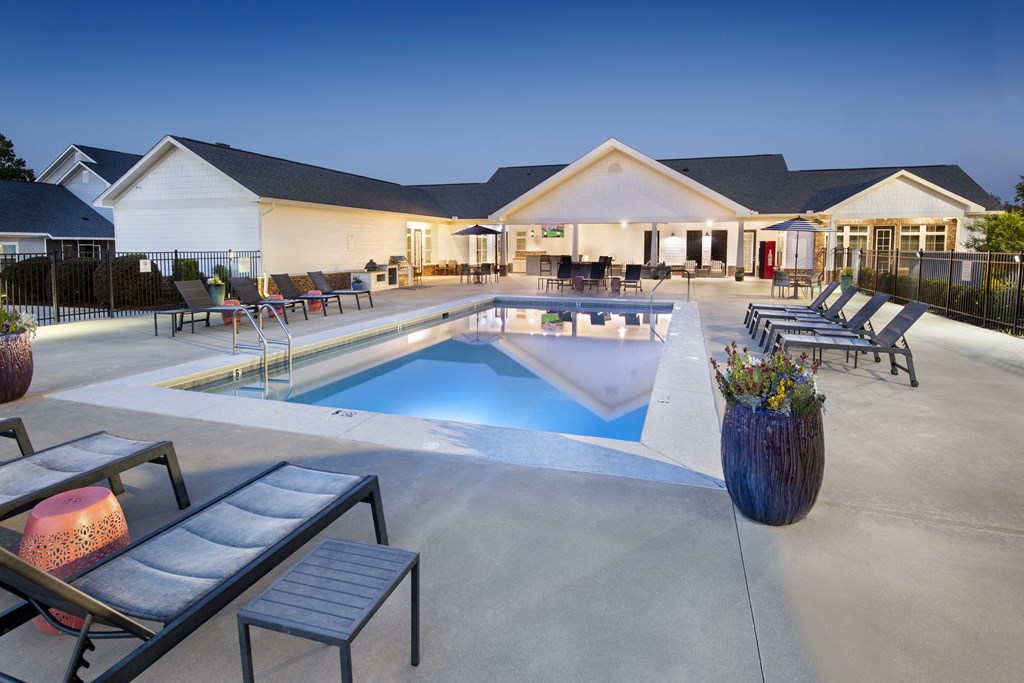 a swimming pool with lounge chairs and tables in front of a house