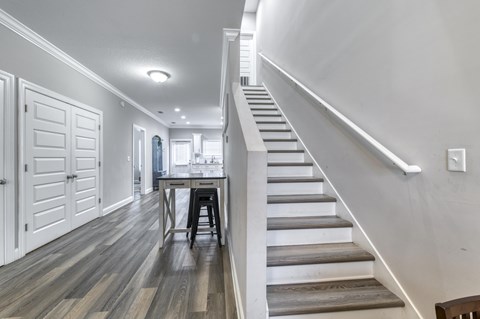 A staircase with a wooden handrail and steps leading to a dining area with a table and chairs.