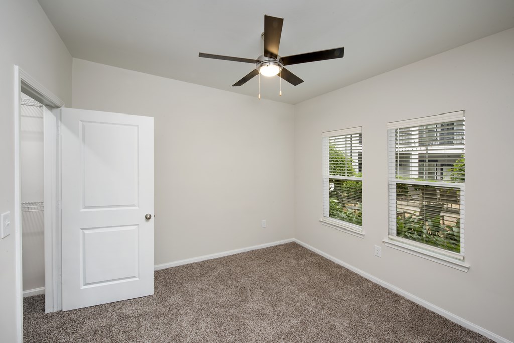 A room with a ceiling fan and two windows.