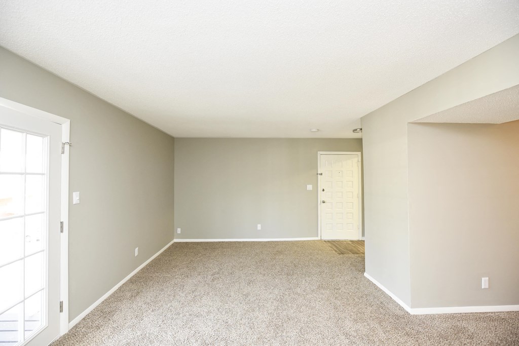 an empty living room with carpet and a door to a closet