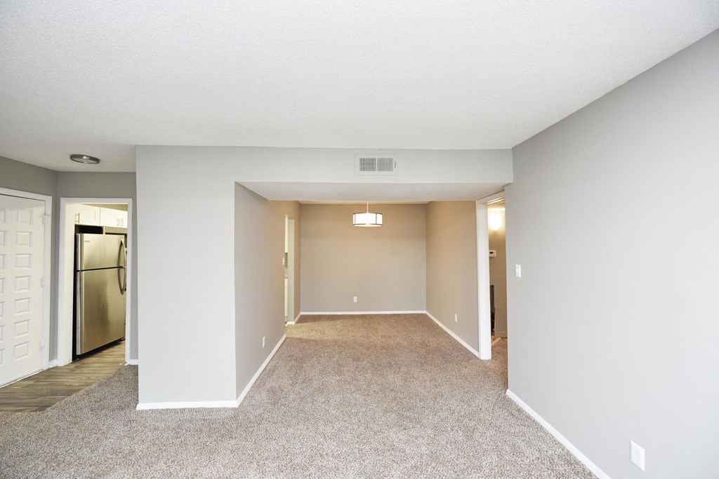 an empty living room with white walls and a stainless steel refrigerator